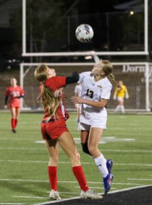 Two female soccer players competing for the ball during a match at night on a field.