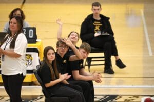 Group of students seated in a gym, clapping and engaging in a sports event.