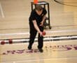 Person playing boccia on an indoor court, focused on throwing a red ball towards a marked area.