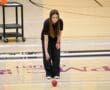 Young woman playing bocce ball indoors on a wooden court, focused and ready to throw.