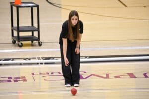 Young woman playing bocce ball indoors on a wooden court, focused and ready to throw.
