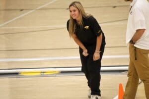 Person in black outfit smiling on a gym floor during sports practice.