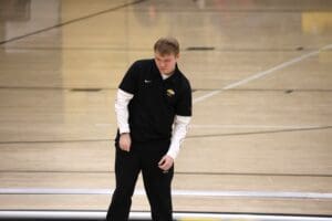 Young man in black athletic wear on an indoor sports court, mid-action.
