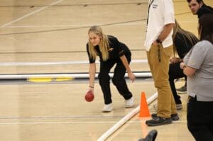 Young woman playing bocce ball indoors at a gymnasium, focused and preparing to roll the ball on the court.