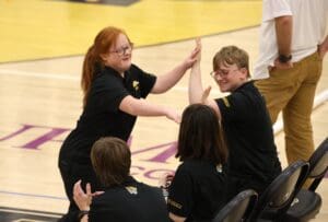 Group of people giving high-fives at a sports arena, wearing matching black shirts, celebrating success.