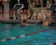 Swimmers at the pool edge during a swim meet, surrounded by starting blocks and spectators.