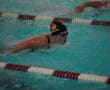Competitive swimmer performing butterfly stroke in pool, wearing goggles and swim cap.