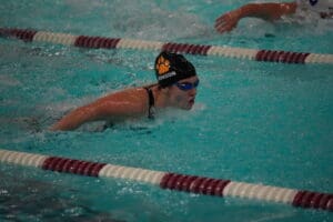 Competitive swimmer performing butterfly stroke in pool, wearing goggles and swim cap.