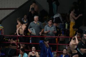 Coaches and swimmers gather poolside at a swim meet, preparing and discussing strategies.