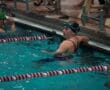 Swimmer resting at poolside during a competition, wearing goggles and swim cap.