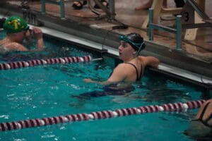 Swimmer resting at poolside during a competition, wearing goggles and swim cap.
