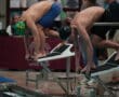 Swimmers in starting position on blocks at indoor swimming competition, ready to dive.