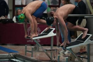 Swimmers in starting position on blocks at indoor swimming competition, ready to dive.