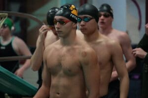Competitive swimmers wearing swim caps and goggles, preparing for a race at an indoor pool event.