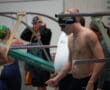 Swimmer prepares before a race, wearing a swim cap and goggles, surrounded by other athletes and coaches.