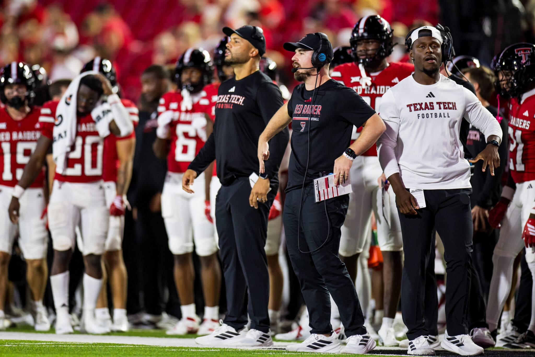 Texas Tech football team and coaches on the sidelines during a game, wearing team uniforms and focused on the field.