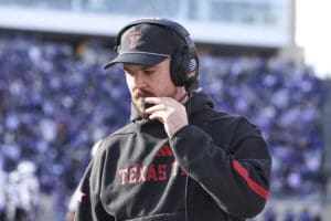 Football coach wearing Texas Tech gear and a headset during a game, intensely focused on the field.