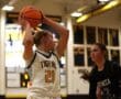 Basketball player in white jersey prepares to pass during indoor game against opponent in black jersey.
