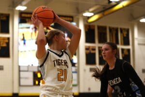 Basketball player in white jersey prepares to pass during indoor game against opponent in black jersey.