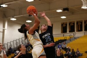 Two basketball players compete near the hoop in a high school game, with a player in white shooting.