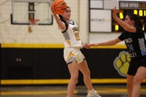 Girls' basketball game action, player in midair pass against defender on school gym court.