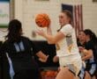 Female basketball player in white uniform prepares to pass during a game.