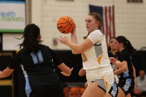 Female basketball player in white uniform prepares to pass during a game.