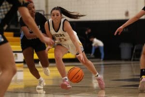 Girls' high school basketball game, player in white uniform dribbling past opponent on the court.