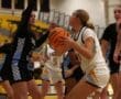 Girls basketball game action shot, player in white attempting a shot, defended by player in black jersey.