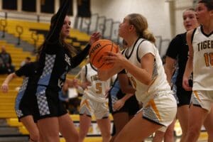 Girls basketball game action shot, player in white attempting a shot, defended by player in black jersey.