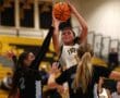 Female basketball player jumps for a shot while guarded by two opponents in a competitive game.