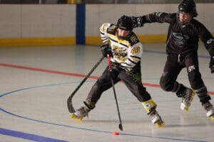 Inline hockey players in action on the rink, wearing helmets and skates, competing for the puck.