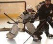 Roller hockey goalie defending the goal during a match, with players in action at the rink.