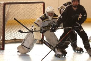 Roller hockey goalie defending the goal during a match, with players in action at the rink.