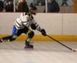 Roller hockey player in action, wearing a white jersey, maneuvering the puck on the rink with spectators in the background.