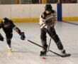 Two inline hockey players compete for the puck on an indoor rink.