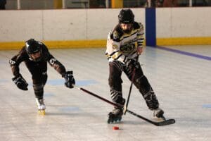 Two inline hockey players compete for the puck on an indoor rink.