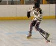 Roller hockey player in action, skating with puck on indoor rink, wearing black helmet and yellow jersey.