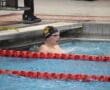 Swimmer finishes race in a pool lane, wearing goggles and a swim cap, with water splashing around.