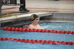 Swimmer finishes race in a pool lane, wearing goggles and a swim cap, with water splashing around.
