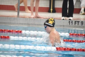 Swimmer in a pool competes in a race, wearing goggles and a swim cap, with a focus on technique.