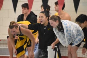 Excited swim team cheering poolside during a competitive swim meet indoors.