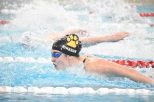 Swimmer in goggles and cap competes in butterfly stroke at indoor pool, creating splashes.
