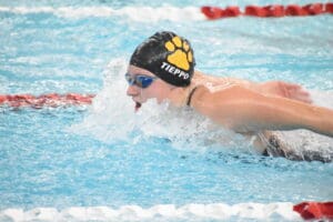 Swimmer performing butterfly stroke in competitive pool wearing black swim cap and goggles.