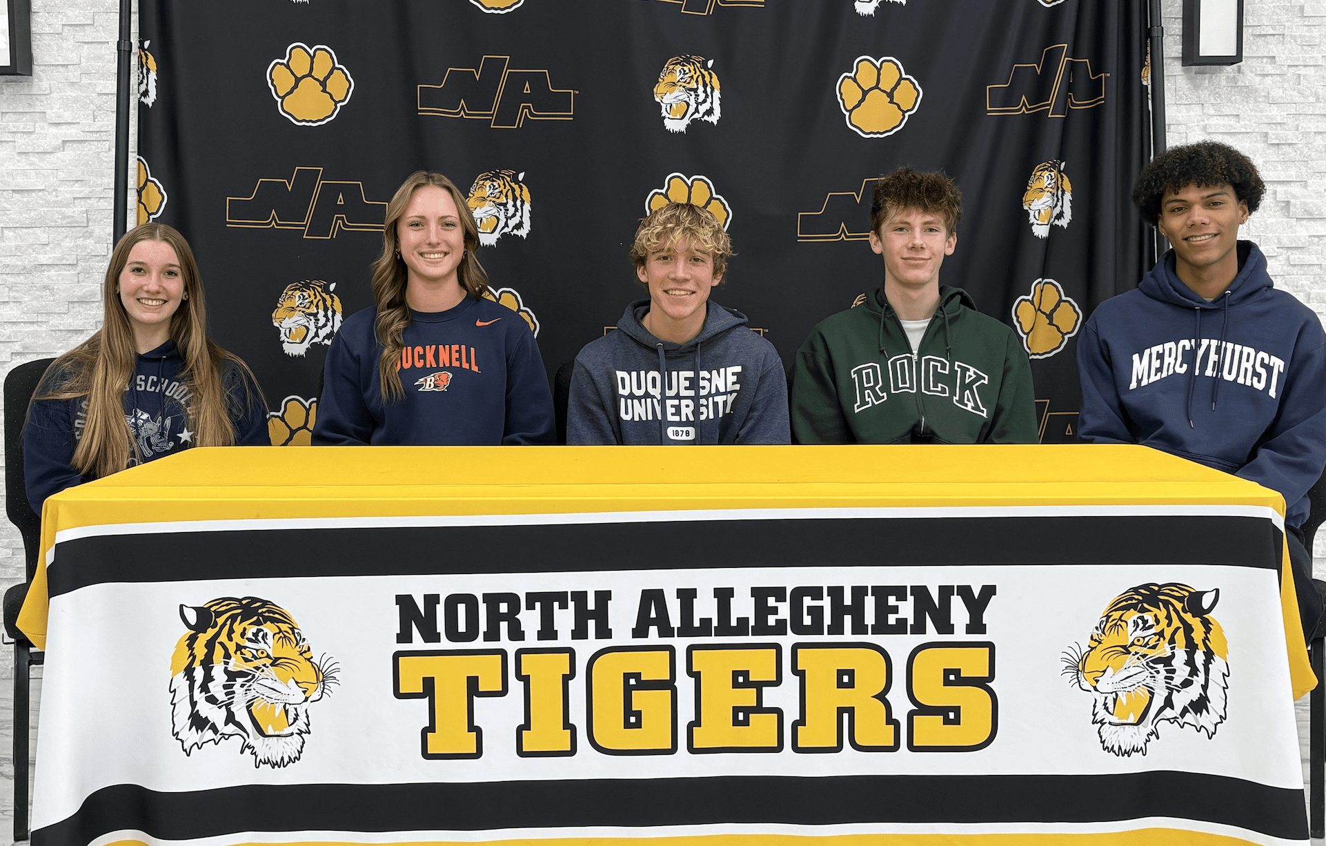Five students pose in college hoodies at North Allegheny Tigers signing day event.