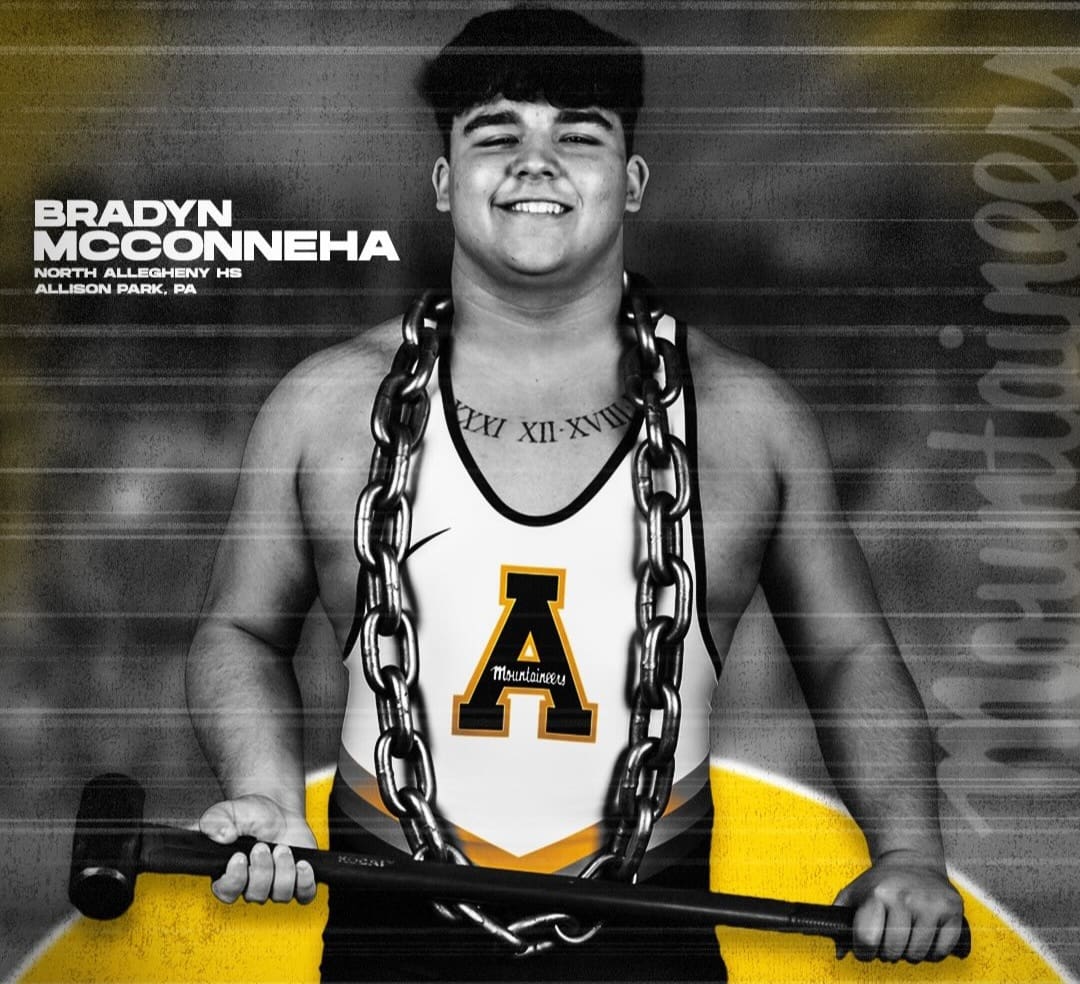 Smiling wrestler in Mountaineers singlet with a chain and sledgehammer, showcasing strength and team pride.