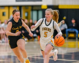 High school basketball game action with player dribbling and opponent in pursuit.