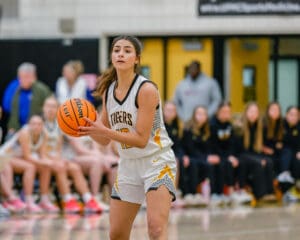 Female basketball player from the Tigers team prepares to make a pass during a game in a gymnasium.
