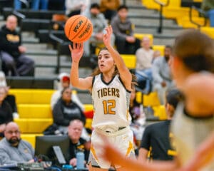 Female basketball player in Tigers jersey number 12 making a jump shot during a game in a gymnasium.