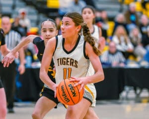 Female basketball player in white Tigers jersey driving towards the hoop during a game.